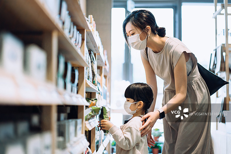 戴着防护口罩在有机食品店购物的年轻亚洲母亲和可爱的小女儿图片素材