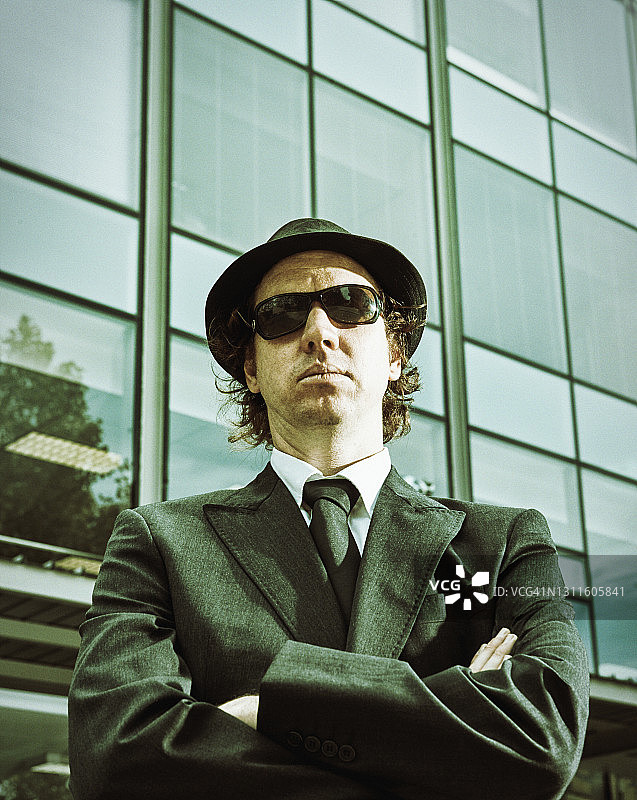 戴帽子和墨镜的黑帮商人威胁性地盯着现代办公楼图片素材