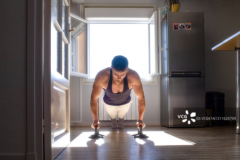 穿背心的年轻男人在厨房里做俯卧撑图片素材