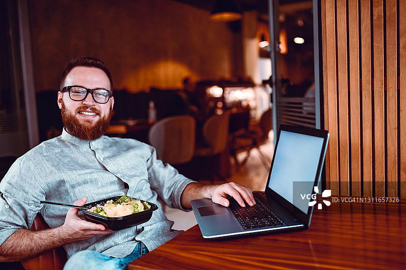 笑容满面的自由职业者准备工作，享用外卖沙拉午餐和笔记本电脑图片素材