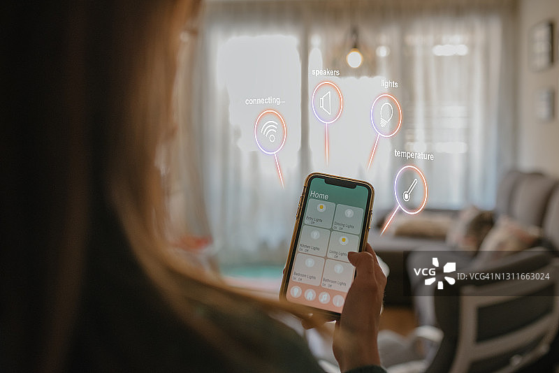 年轻女子在家使用手机远程控制智能家居特写：物联网和家庭自动化概念图片素材