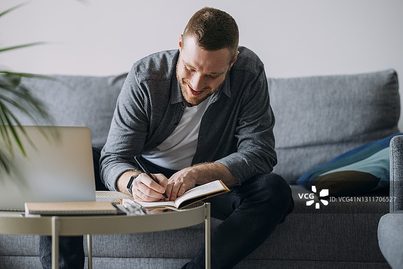 在家工作：男人坐在沙发上用笔记本电脑写笔记图片素材