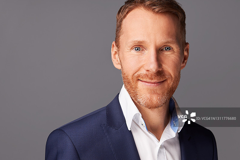 四十多岁红发胡须男士的肖像照，身穿白衬衫和蓝色夹克，在灰色背景的影棚中拍摄图片素材