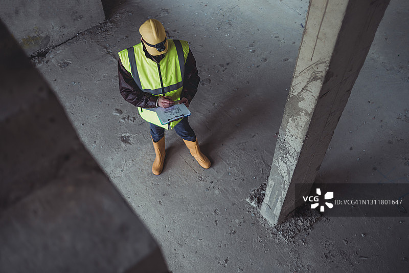 工程师在建筑工地阅读计划的人像。一位戴着安全帽、穿着安全背心的土木工程师使用平板电脑。致力于建筑改造和投资评估。图片素材