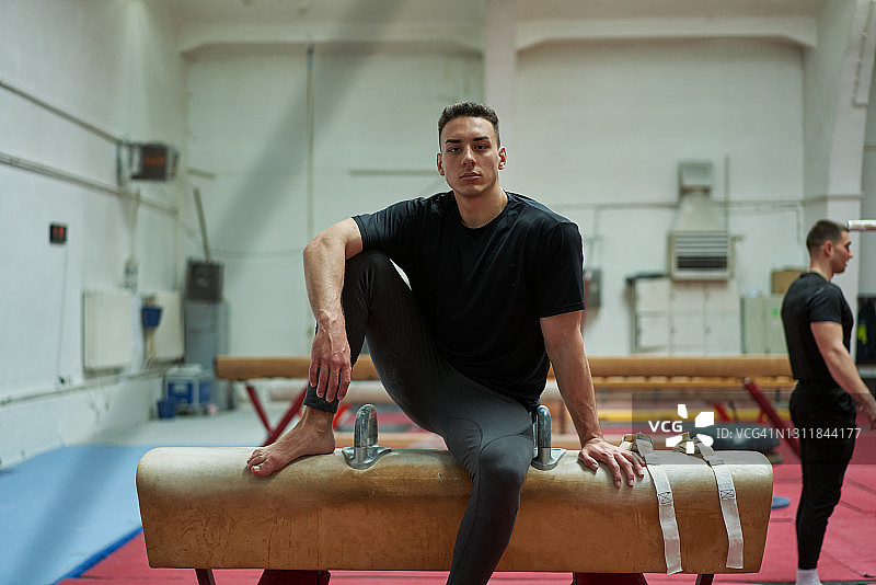 完成高强度体操训练后，坐在鞍马上休息的严肃男体操运动员图片素材