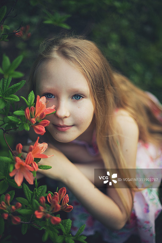 学龄女孩在盛开的公园里，穿着粉红色的连衣裙，闻着花香图片素材