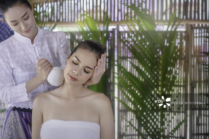 在明亮的水疗沙龙中享受草药球按摩的亚洲白皮肤美女图片素材
