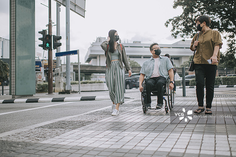 坐在轮椅上的中国籍亚洲男子在吉隆坡与朋友们过马路图片素材
