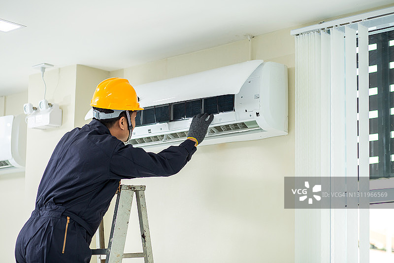 空调技术员：男性技术员身穿安全制服在室内维修空调图片素材