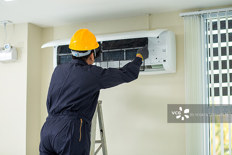 空调技术员：男性技术员身穿安全制服在室内维修空调图片素材