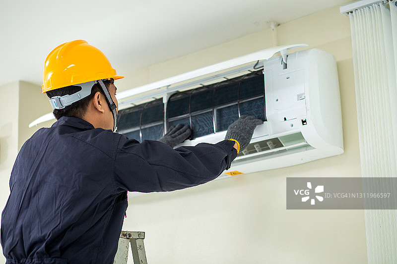 空调技术员：男性技术员身穿安全制服在室内维修空调图片素材