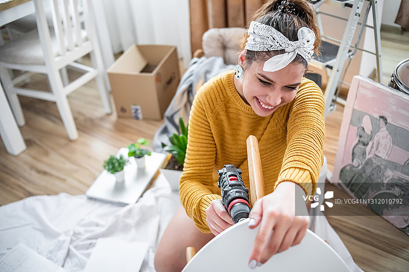 年轻女子搬进新公寓，用无线螺丝刀组装客厅桌子图片素材