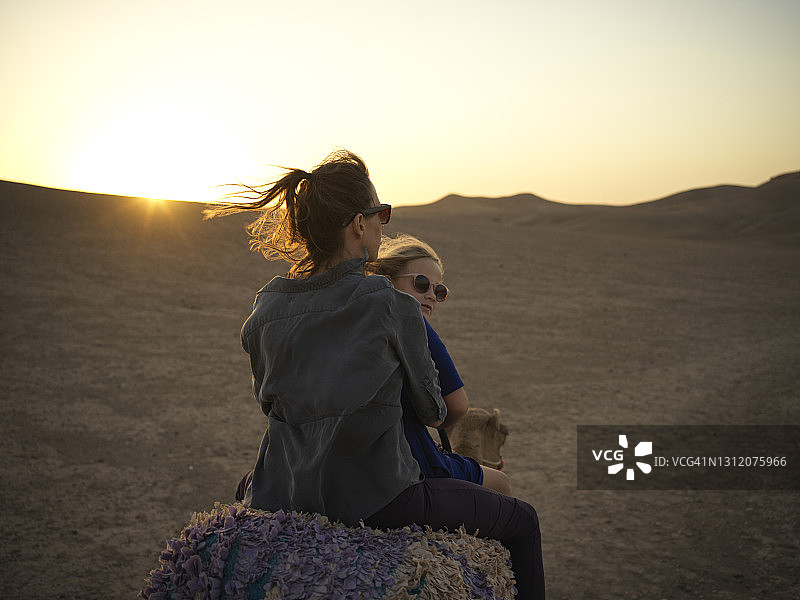 日落时分，母女在摩洛哥骑着骆驼穿过沙漠图片素材