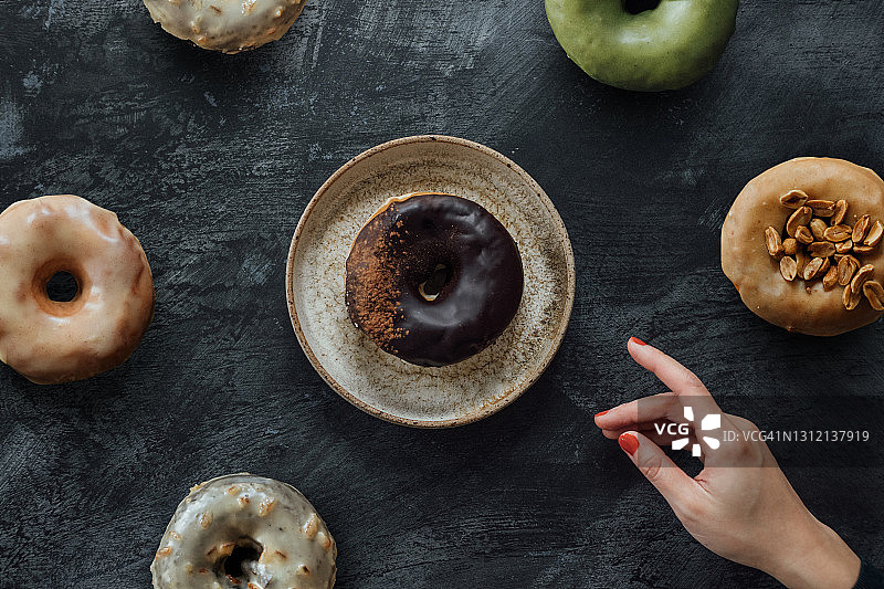 女性手拿各种美食甜甜圈的2.5D复古深色背景拍摄图片素材