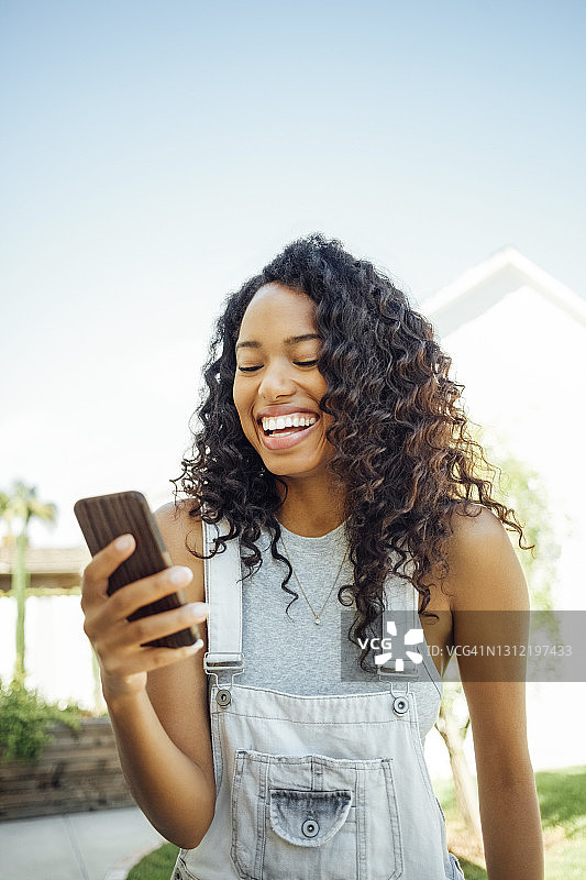 快乐的女人对着晴朗的天空看智能手机图片素材