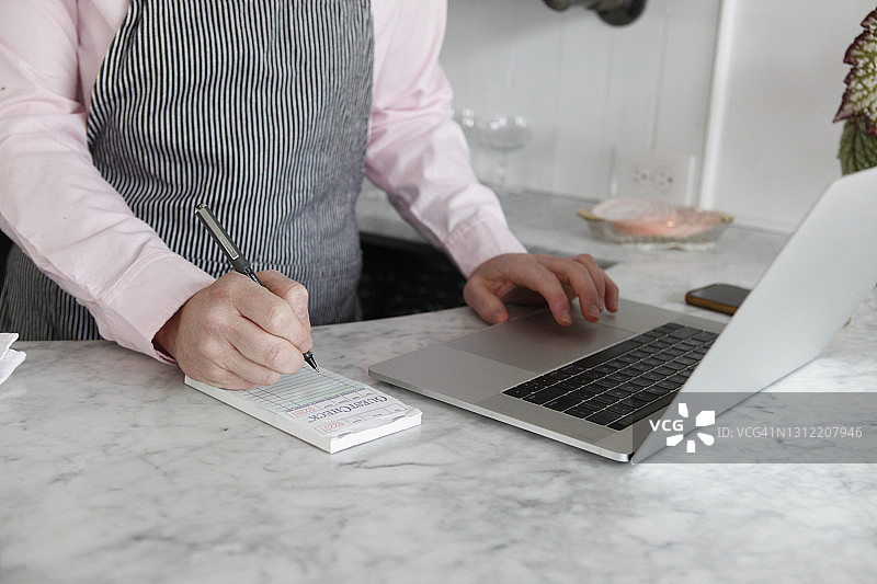 男人在吧台用笔记本电脑工作并用笔写作的特写图片素材