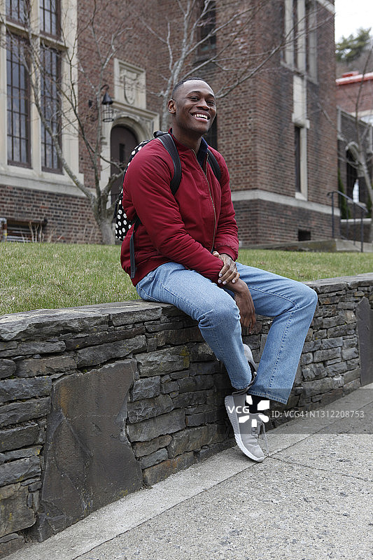 坐在校园墙上的微笑大学生肖像图片素材
