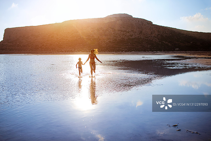日落时分，男孩和他的母亲在水中奔跑图片素材