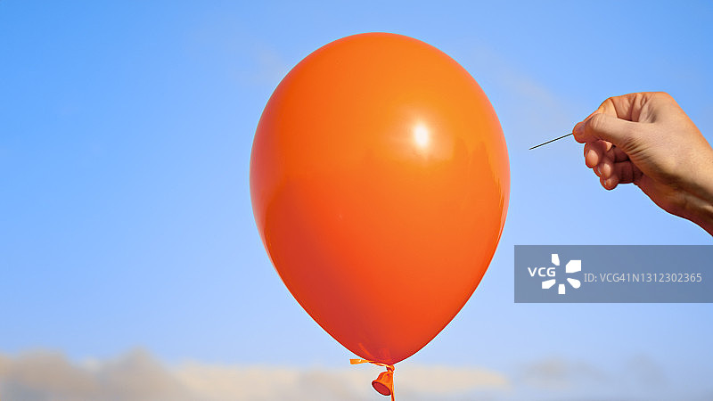 男人用别针刺破橙色气球图片素材