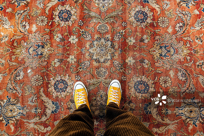穿着黄色帆布鞋的男人站在旧地毯上，高角度个人视角图片素材