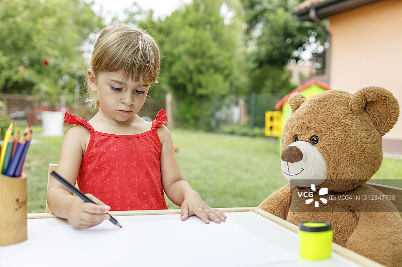 女孩在户外绘画，泰迪熊在身边图片素材