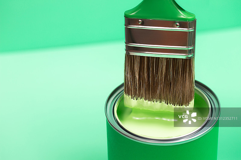 画笔浸在粉彩翠绿色背景上的绿色油漆桶中，家居室内重新装修概念，俯视特写图片素材