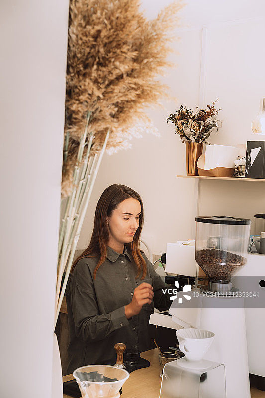 身穿绿色亚麻衬衫的年轻女咖啡师在现代简约咖啡店的吧台后打奶泡图片素材