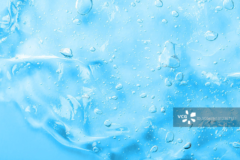 蓝色背景上的透明液体精华液，含保湿玻尿酸，带气泡的抗菌凝胶，化妆和护肤美容产品图片素材