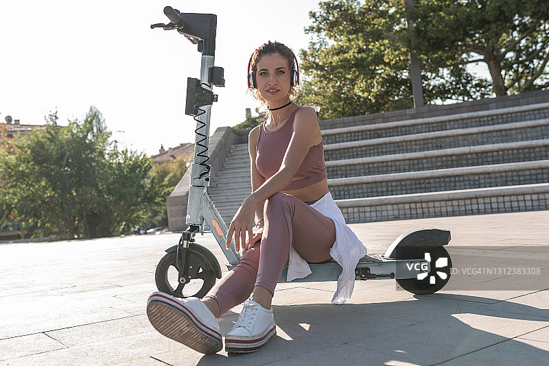 年轻漂亮的女人在夏日街头夕阳下骑着电动滑板车图片素材