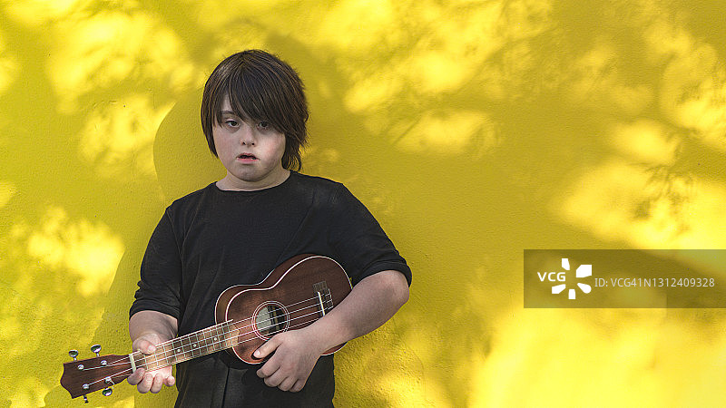 患有唐氏综合征的儿童在黄色背景下弹奏尤克里里图片素材