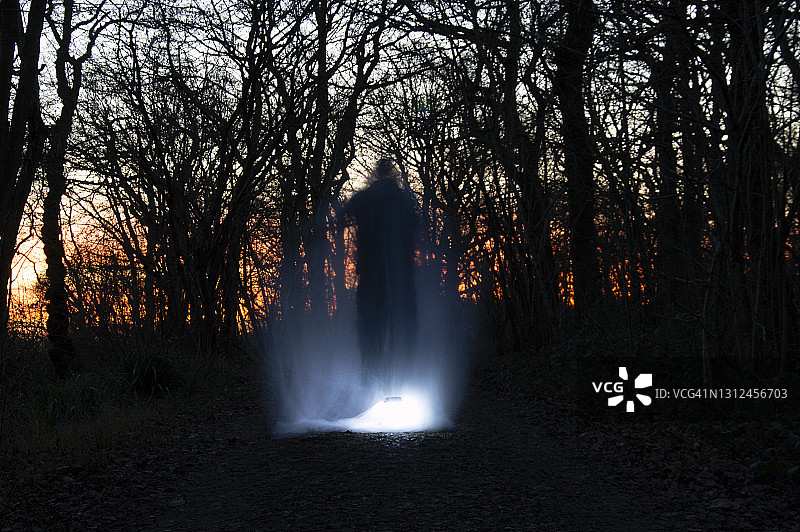 恐怖概念：黑暗冬季森林日落后，灯光环绕的模糊幽灵身影图片素材