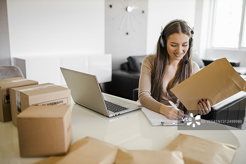 在网上商店工作的女人，穿着休闲服装，在笔记本电脑上查看客户地址和包裹信息图片素材