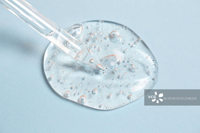 滴管滴出凝胶或精华液，带有气泡，淡蓝色背景图片素材