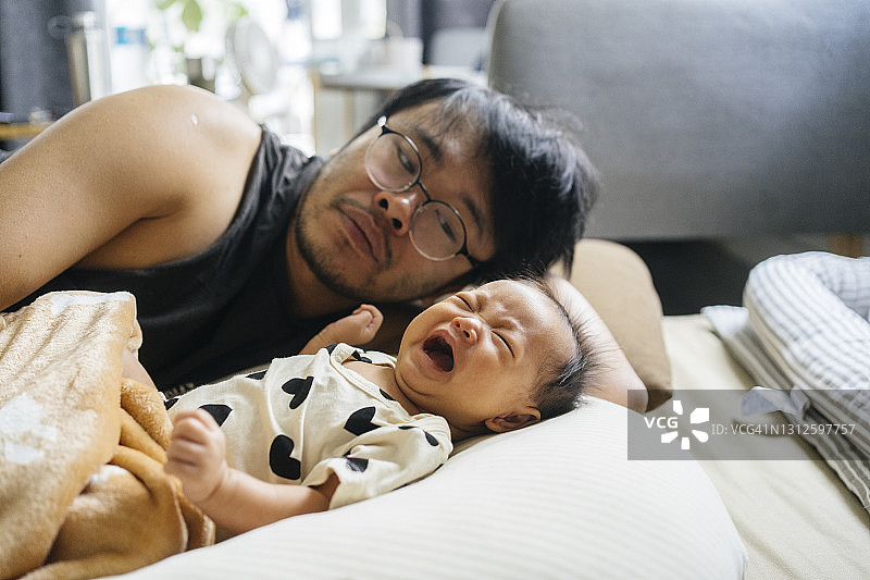 给新生女儿喂食和拍嗝后，因女儿哭闹而感到吵闹的亚洲单身父亲图片素材