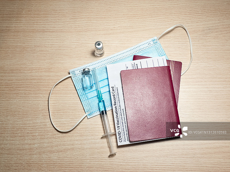 疫苗接种记录卡、护照、装有新冠病毒疫苗的小瓶。木桌上的注射器和口罩，特写，复制空间。免疫护照，无风险概念。图片素材