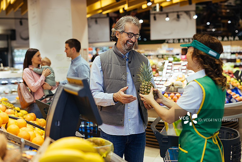 超市员工帮助顾客挑选水果图片素材