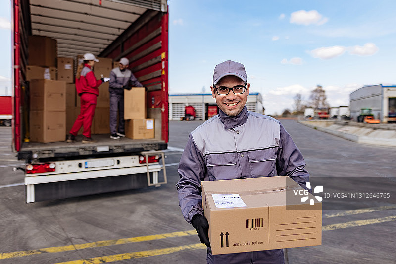 快乐的快递员抱着纸箱看着镜头图片素材