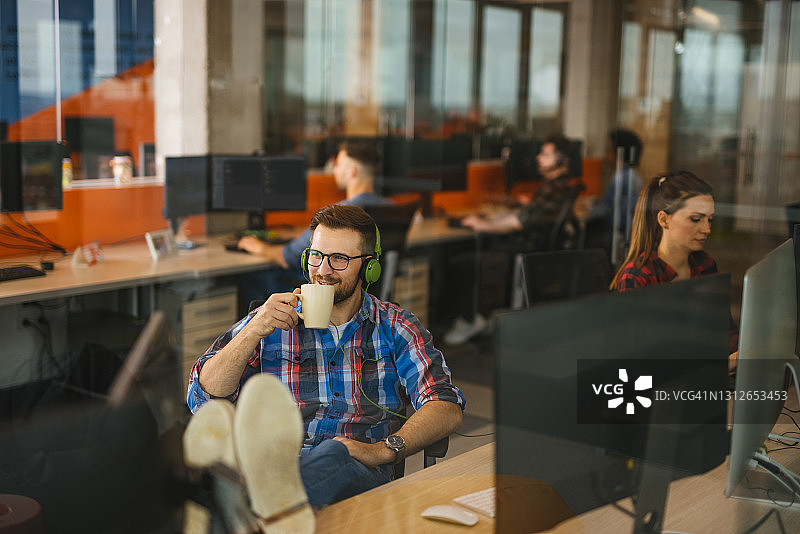 放松的男性计算机程序员在办公室享受音乐和咖啡图片素材