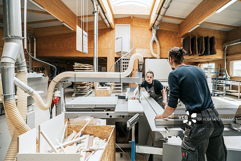 在车间圆锯机上一起工作的年轻木匠图片素材