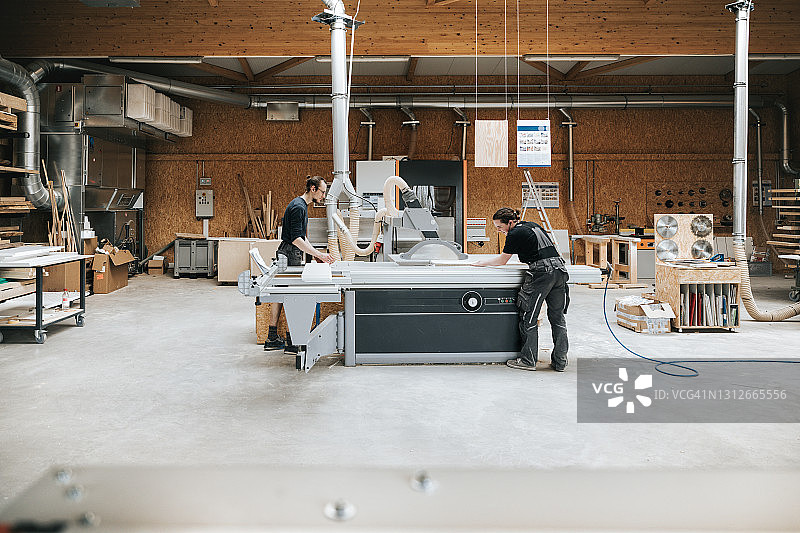 在车间圆锯机上一起工作的年轻木匠图片素材
