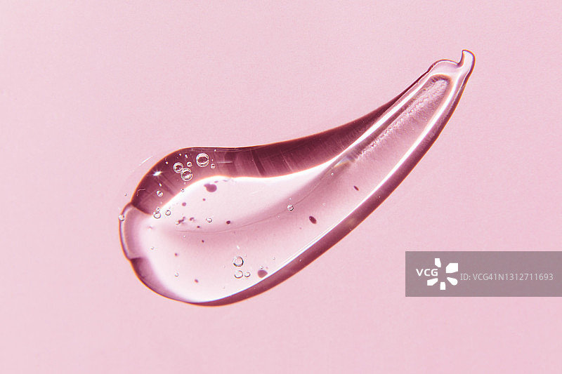 粉色背景上的透明凝胶涂抹，透明质酸液体凝胶图片素材