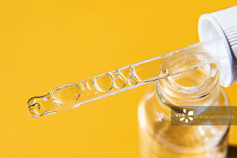 特写：化妆品滴管，含透明质酸、油、维生素、血清，在黄色背景的玻璃瓶中。护肤美容产品图片素材