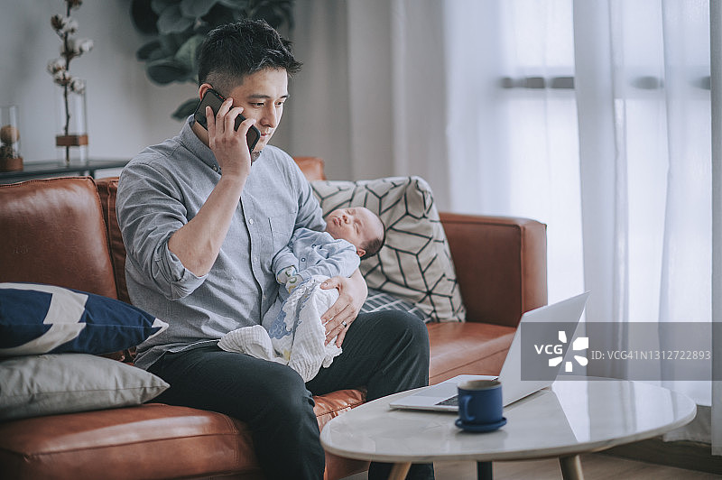在家工作，在客厅沙发上抱着婴儿听电话的中国男人图片素材
