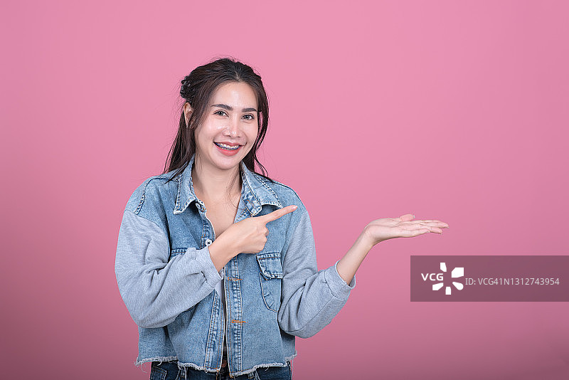 让我向您介绍一下。年轻女子看着张开的手，拿着logo产品，指着手掌上的空白处，展示着什么，粉色背景图片素材