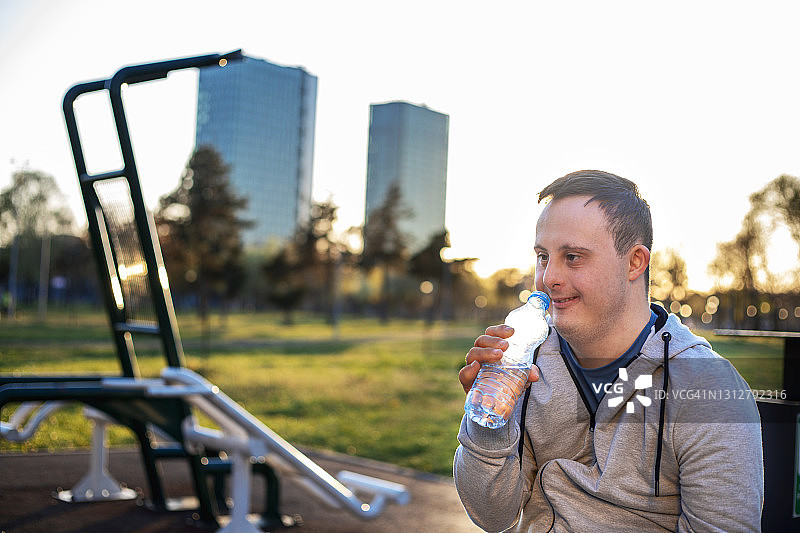 患有唐氏综合征的年轻男子在公共公园的户外健身房锻炼图片素材