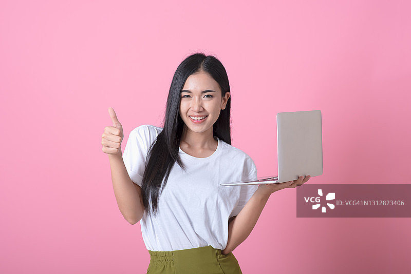 在粉色背景上用笔记本电脑工作的快乐亚洲女商人图片素材