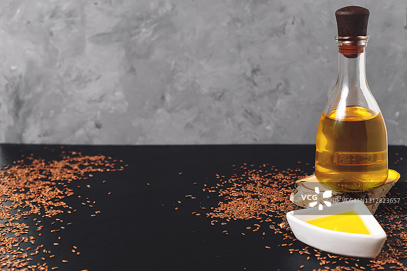 白色碗里的亚麻籽和玻璃瓶装亚麻籽油，在深灰色背景的木制砧板上图片素材
