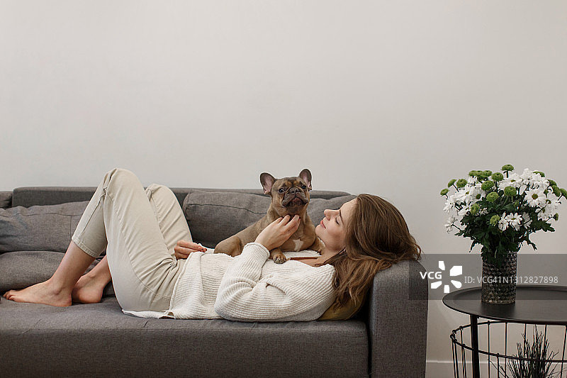 年轻女子抚摸着躺在沙发上的斗牛犬图片素材