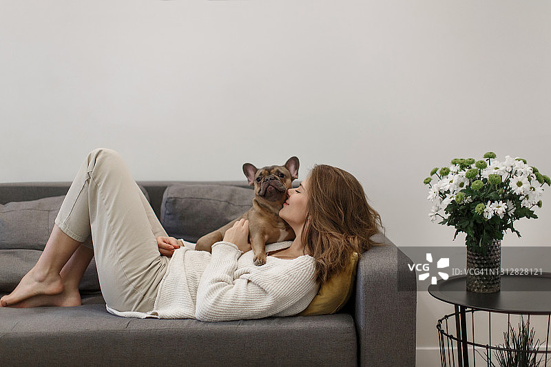 快乐的年轻女子在沙发上拥抱她的狗图片素材