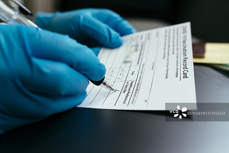 医生戴着手术手套，出示疫苗接种卡和护照，证明已接种第一剂新冠疫苗图片素材